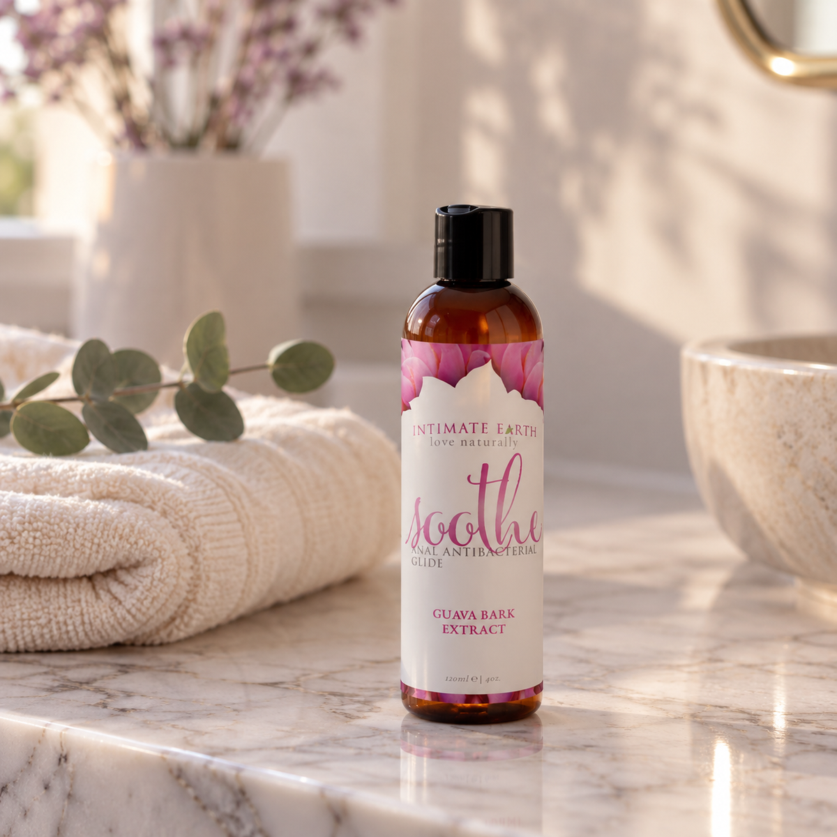 Fles Intimate Earth Soothe op een marmeren badkamerblad naast een handdoek en eucalyptus