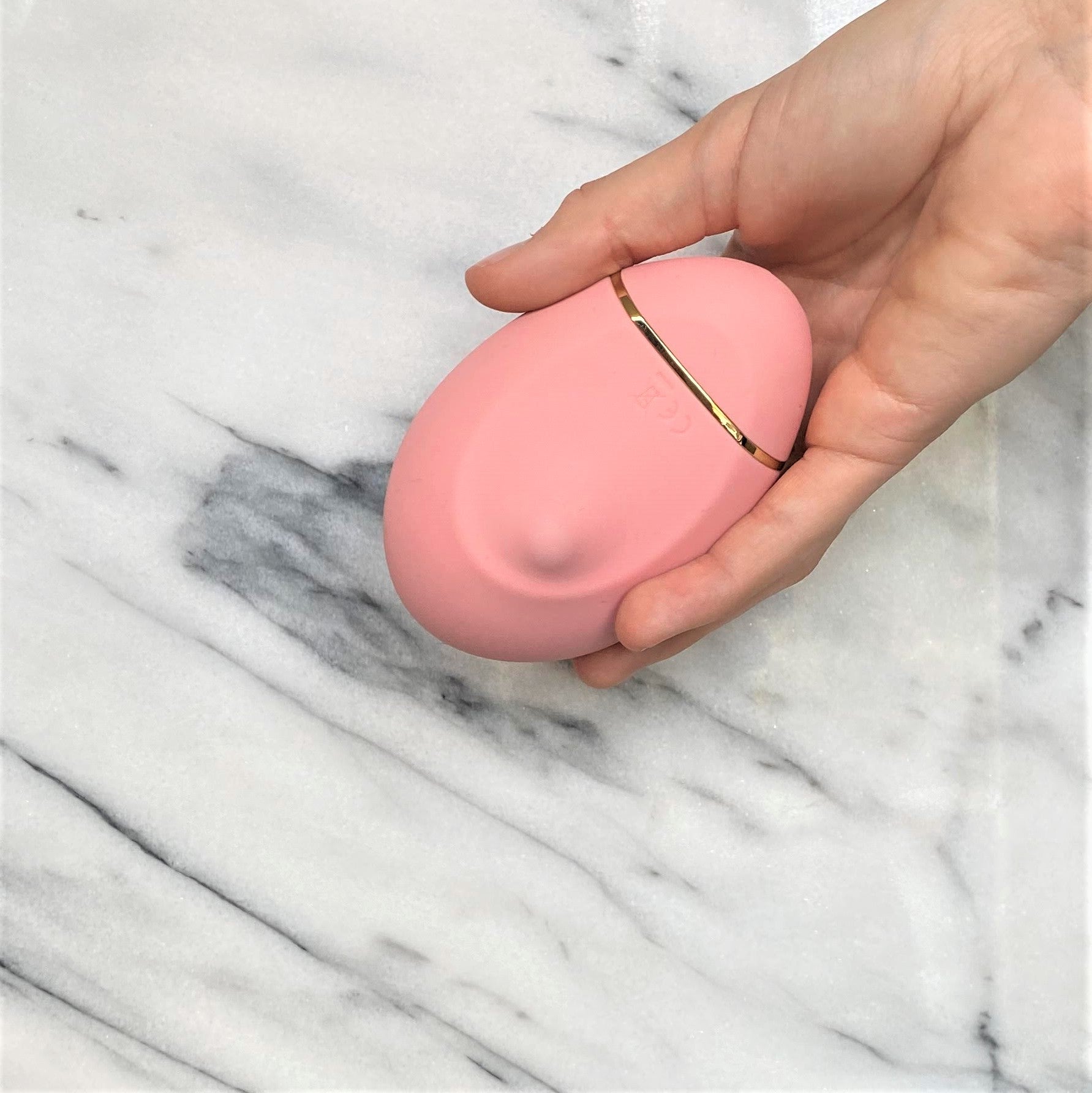 Roze siliconen clitoris vibrator met gouden accent in hand, compact lay-on design