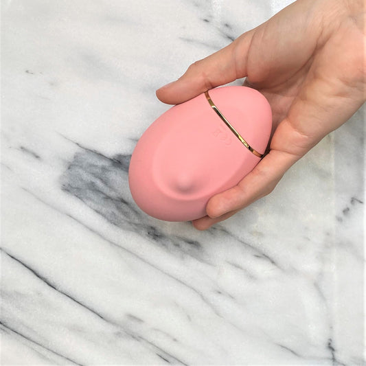 Roze siliconen clitoris vibrator met gouden accent in hand, compact lay-on design