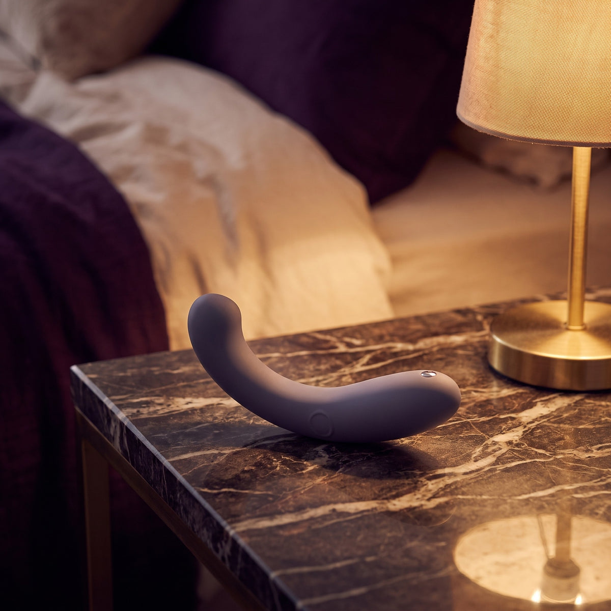 Sfeerbeeld: paarse G-Kii g-spot vibrator op een donker nachtkastje bij warm lamplicht