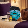 Sfeerbeeld: Kama Sutra Getaway Kit op een hotelbed naast een weekendtas en een brandend theelichtje