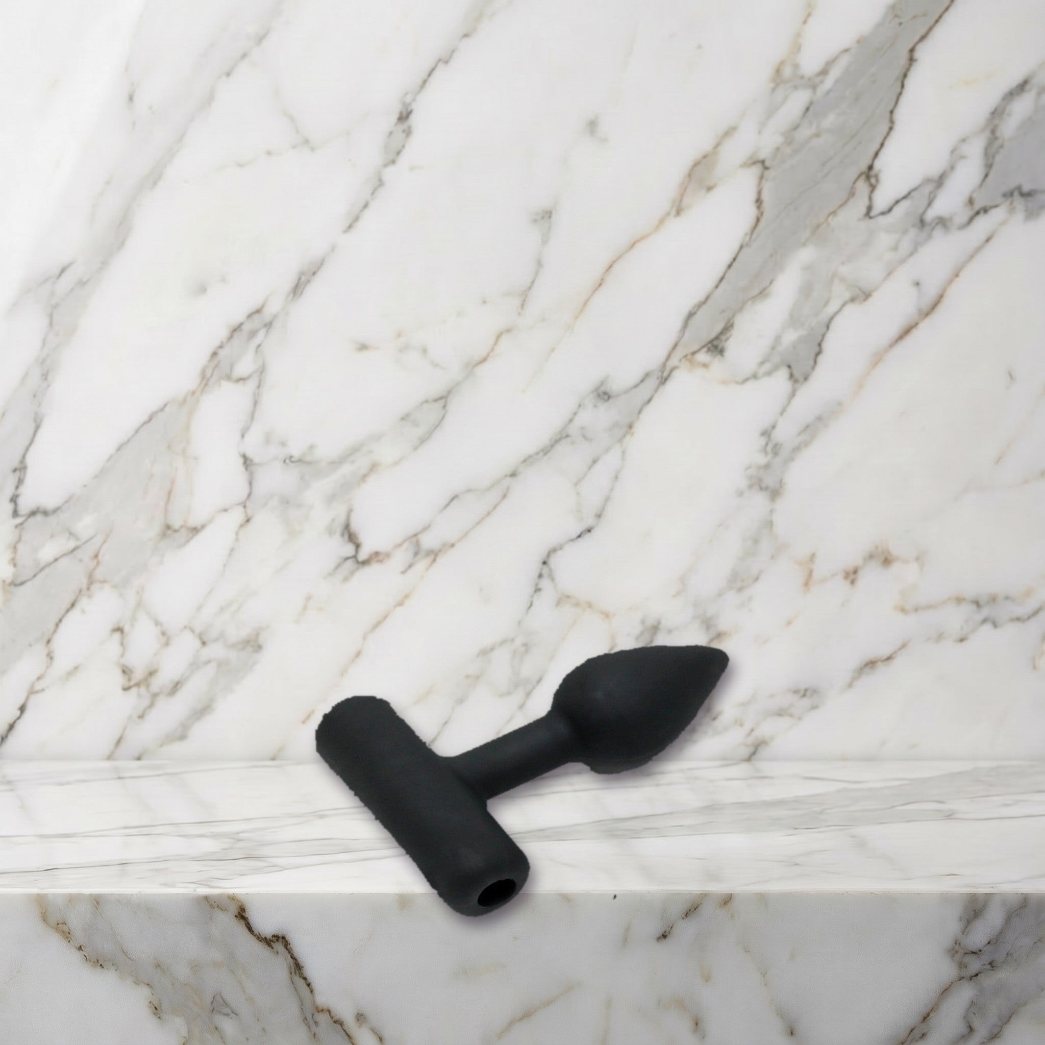 Kleine zwarte siliconen buttplug maat XS liggend op een marmeren plank