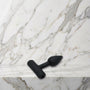 Kleine zwarte siliconen buttplug maat XS liggend op een marmeren plank