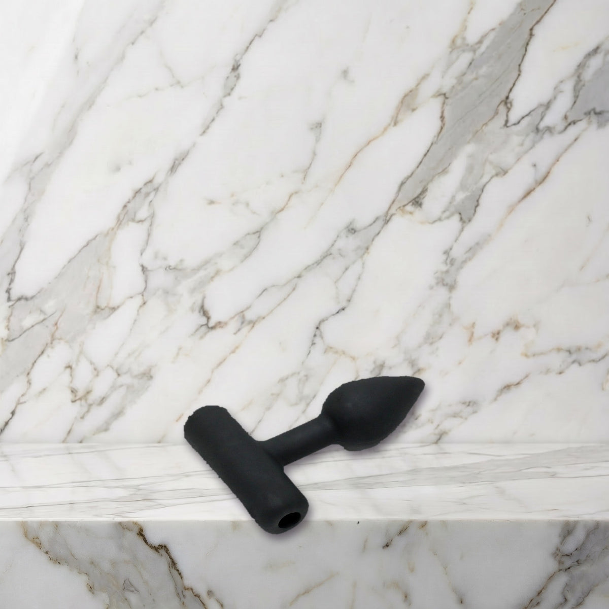 Kleine zwarte siliconen buttplug maat XS liggend op een marmeren plank