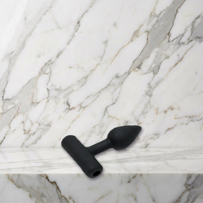 Kleine zwarte siliconen buttplug maat XS liggend op een marmeren plank