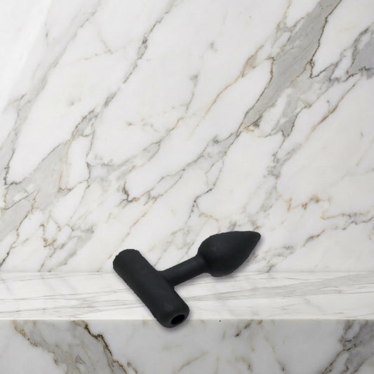Kleine zwarte siliconen buttplug maat XS liggend op een marmeren plank