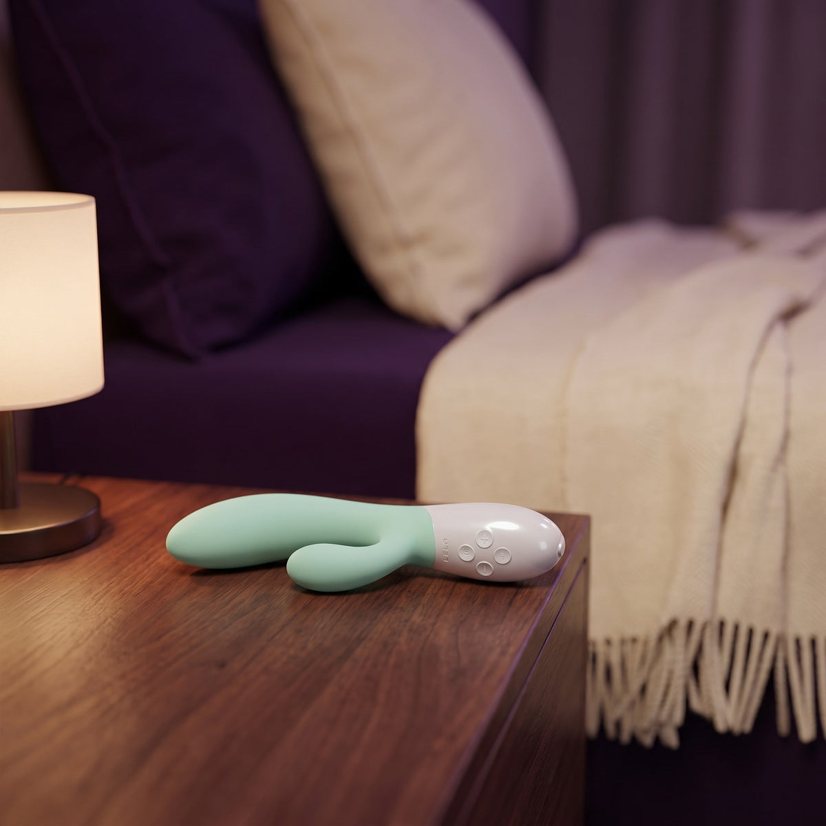 Sfeerbeeld: Ina 3 in licht groen op een houten nachtkastje naast een lamp in avondlicht