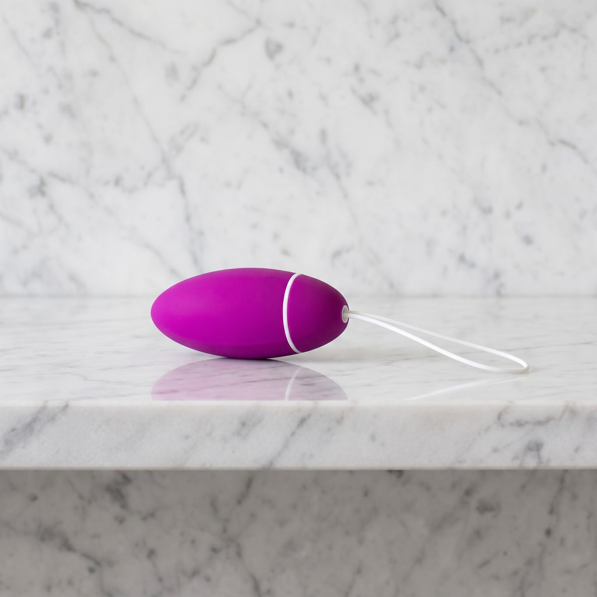 Magenta kegeltrainer met wit koordje op een marmeren plank, LELO Luna Smart Bead