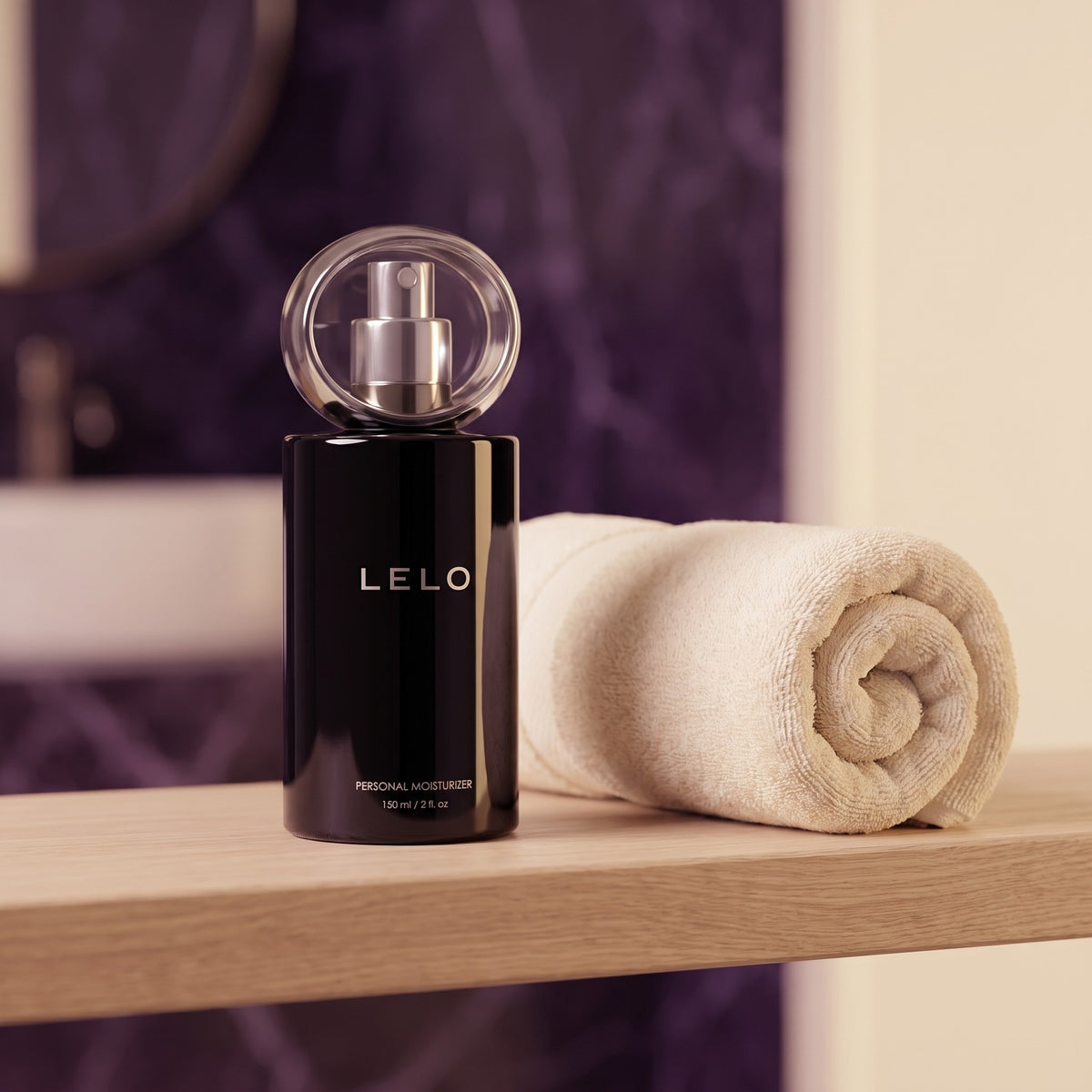 Sfeerbeeld: zwarte fles LELO Personal Moisturizer op een badkamerplank naast een opgerolde handdoek