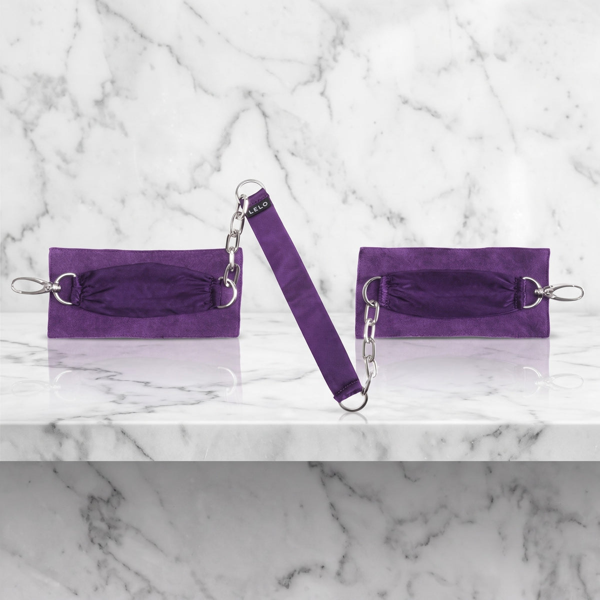 Paarse suède boeien met zijden lint en kettinkjes op een marmeren plank, Sutra Chainlink van LELO