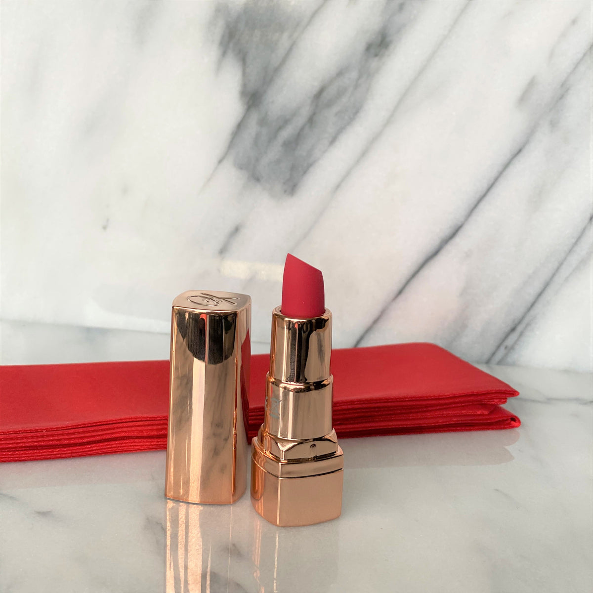 Sfeerbeeld van de lippenstift vibrator met dop naast een rood satijnen lint op marmer