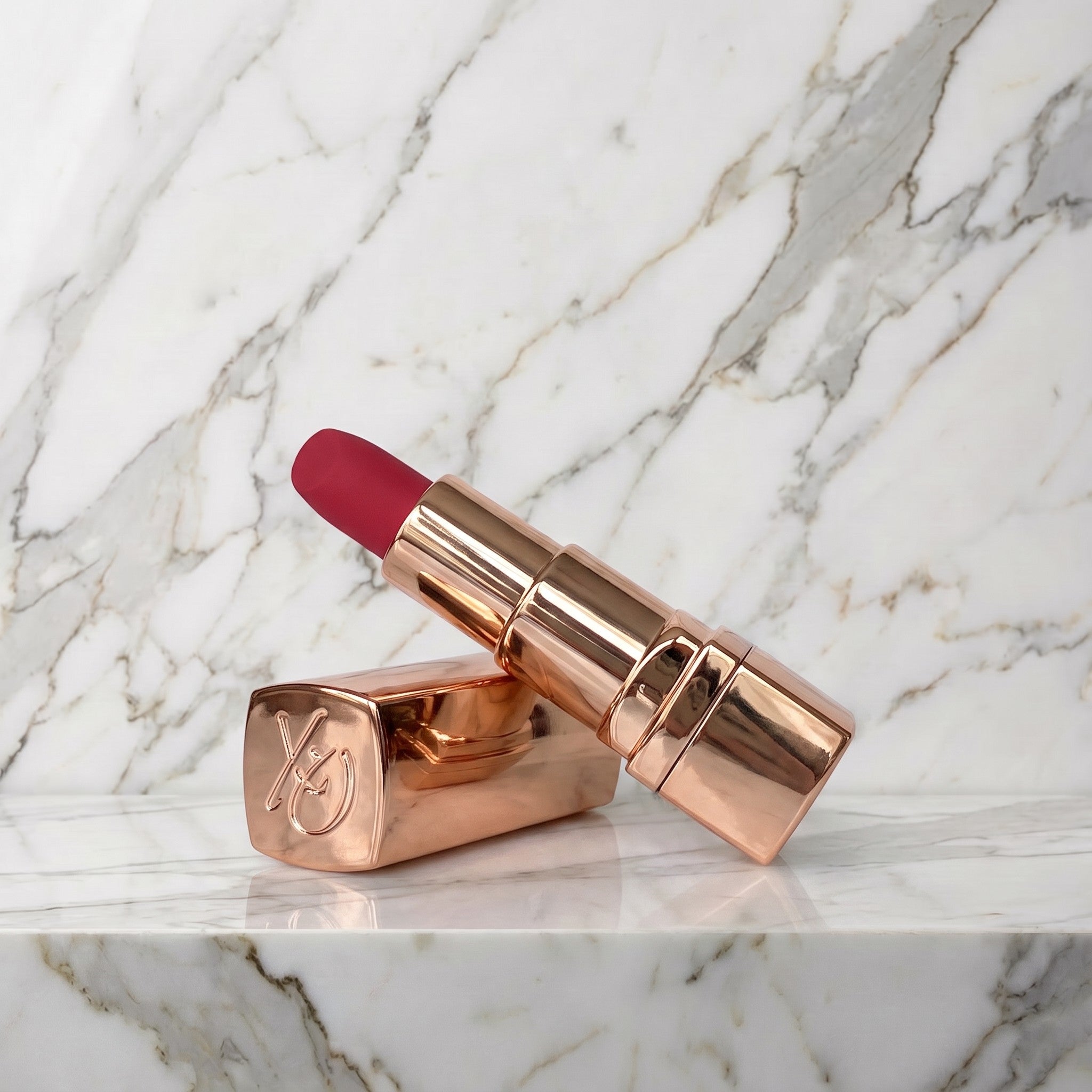 Lippenstift vibrator met roségouden huls en rood topje op een marmeren plank