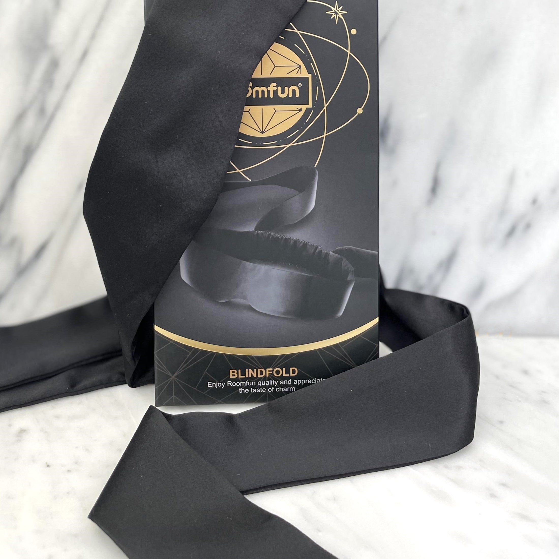 Zwarte satijnen blinddoek naast het zwart met gouden doosje waarin hij geleverd wordt