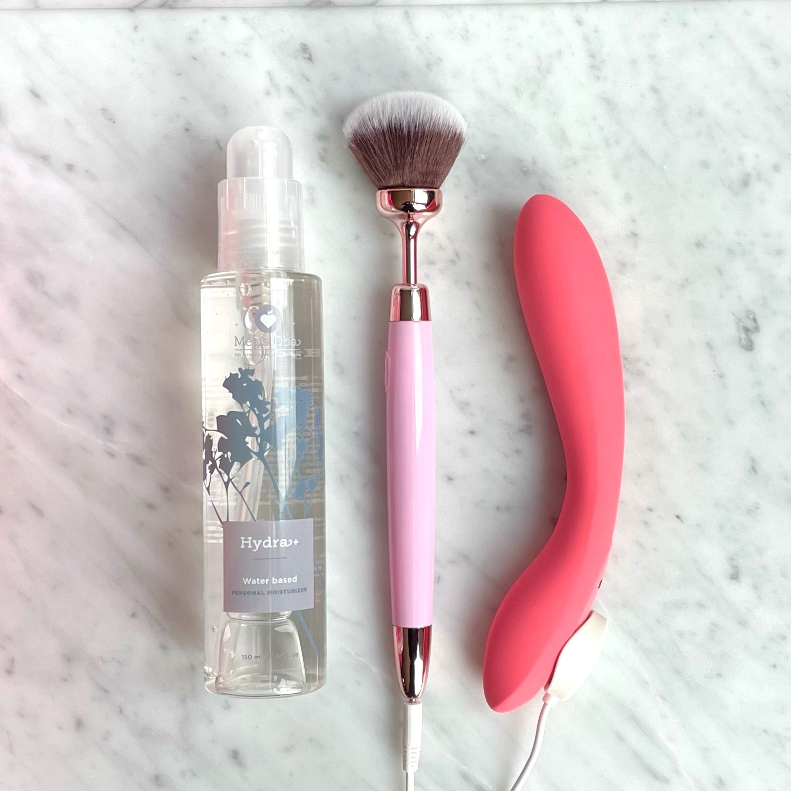 De drie onderdelen van de Gentle Sensations Kit naast elkaar op licht marmer: glijmiddel, vibrerende brush en slanke vibrator