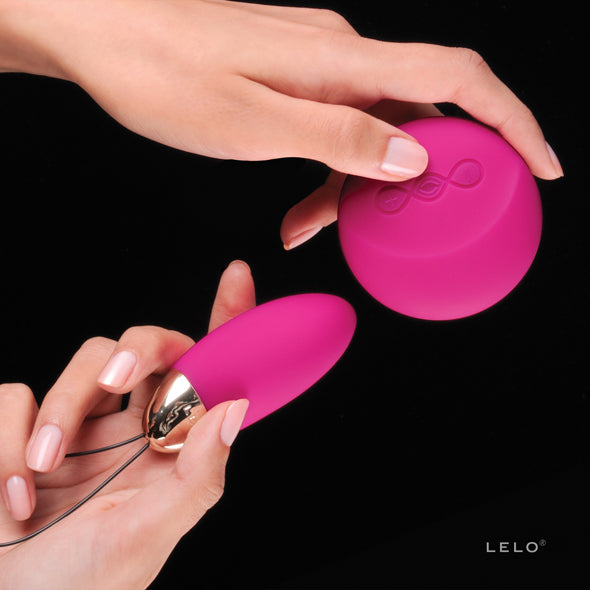 Twee handen houden het roze eitje en de ronde afstandsbediening van de Lelo Lyla 2 vast