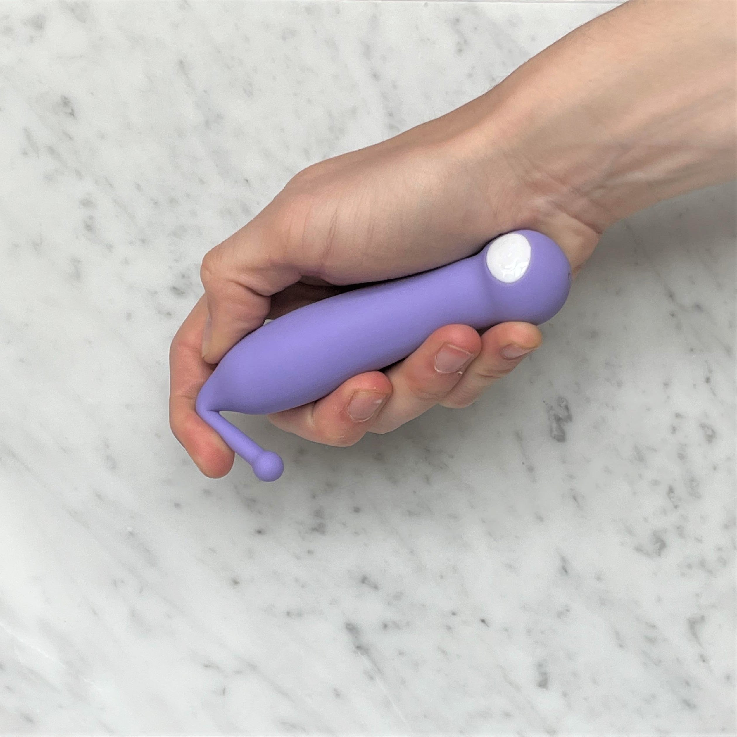 Hand houdt lila clitoris vibrator met smal tipje vast, siliconen materiaal, compact formaat