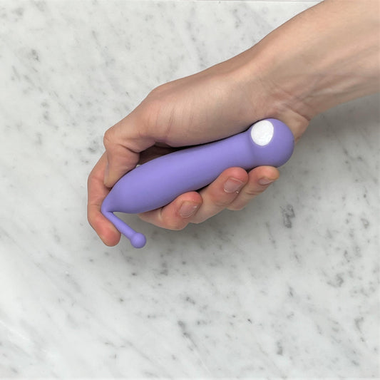 Hand houdt lila clitoris vibrator met smal tipje vast, siliconen materiaal, compact formaat