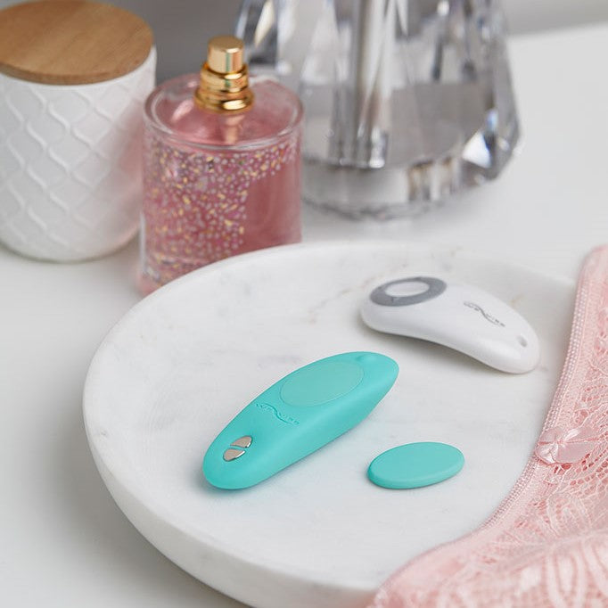 Sfeerbeeld: aqua blauwe We-Vibe Moxie+ met afstandsbediening op een marmeren schaal naast een parfumfles