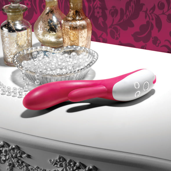 Roze-witte Nexus Femme Bisous rabbit vibrator liggend op sierlijk tafeltje met glazen flesjes en parels