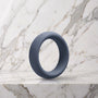 Brede leigrijze siliconen cockring van 40 mm op een marmeren plank, OptiMALE C-Ring
