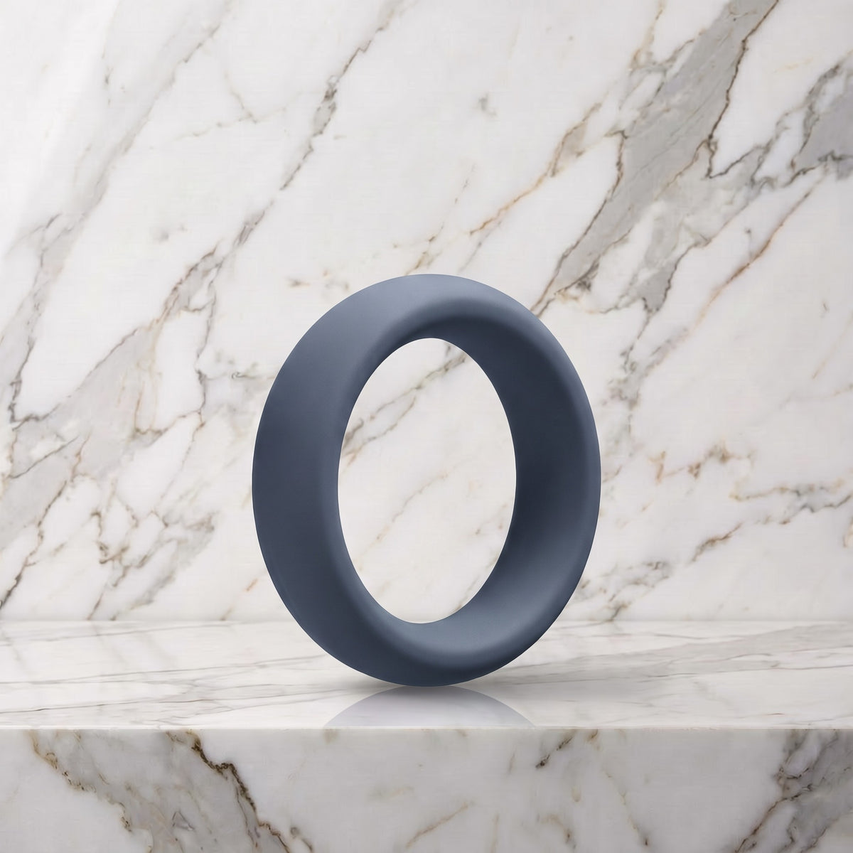 Brede leigrijze siliconen cockring van 40 mm op een marmeren plank, OptiMALE C-Ring