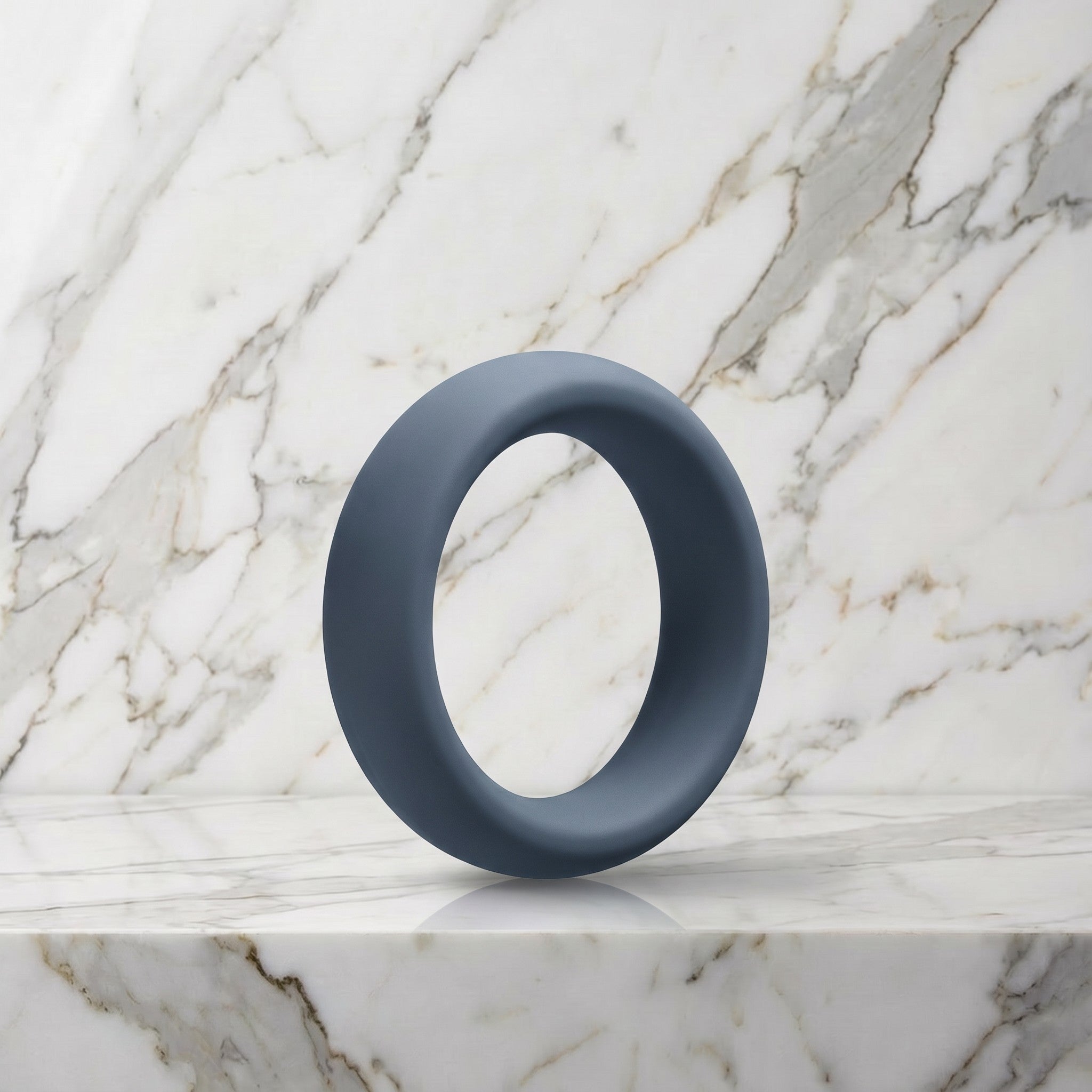Brede leigrijze siliconen cockring van 45 mm op een marmeren plank, OptiMALE C-Ring
