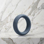 Brede leigrijze siliconen cockring van 45 mm op een marmeren plank, OptiMALE C-Ring
