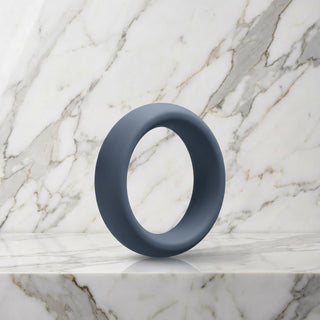 Brede leigrijze siliconen cockring van 45 mm op een marmeren plank, OptiMALE C-Ring