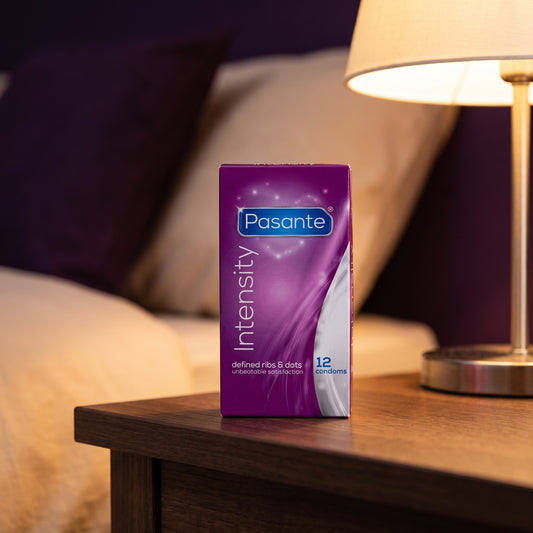 Sfeerbeeld: doosje Pasante Intensity condooms op een houten nachtkastje bij een brandende lamp
