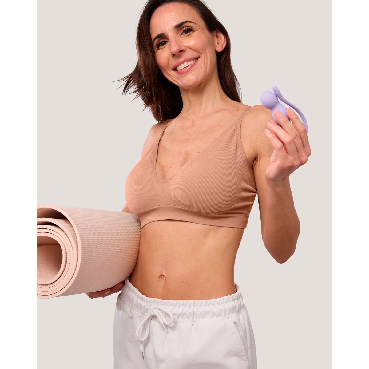 Lachende vrouw met een yogamat onder de arm houdt de lila trainer omhoog, Perifit Care+