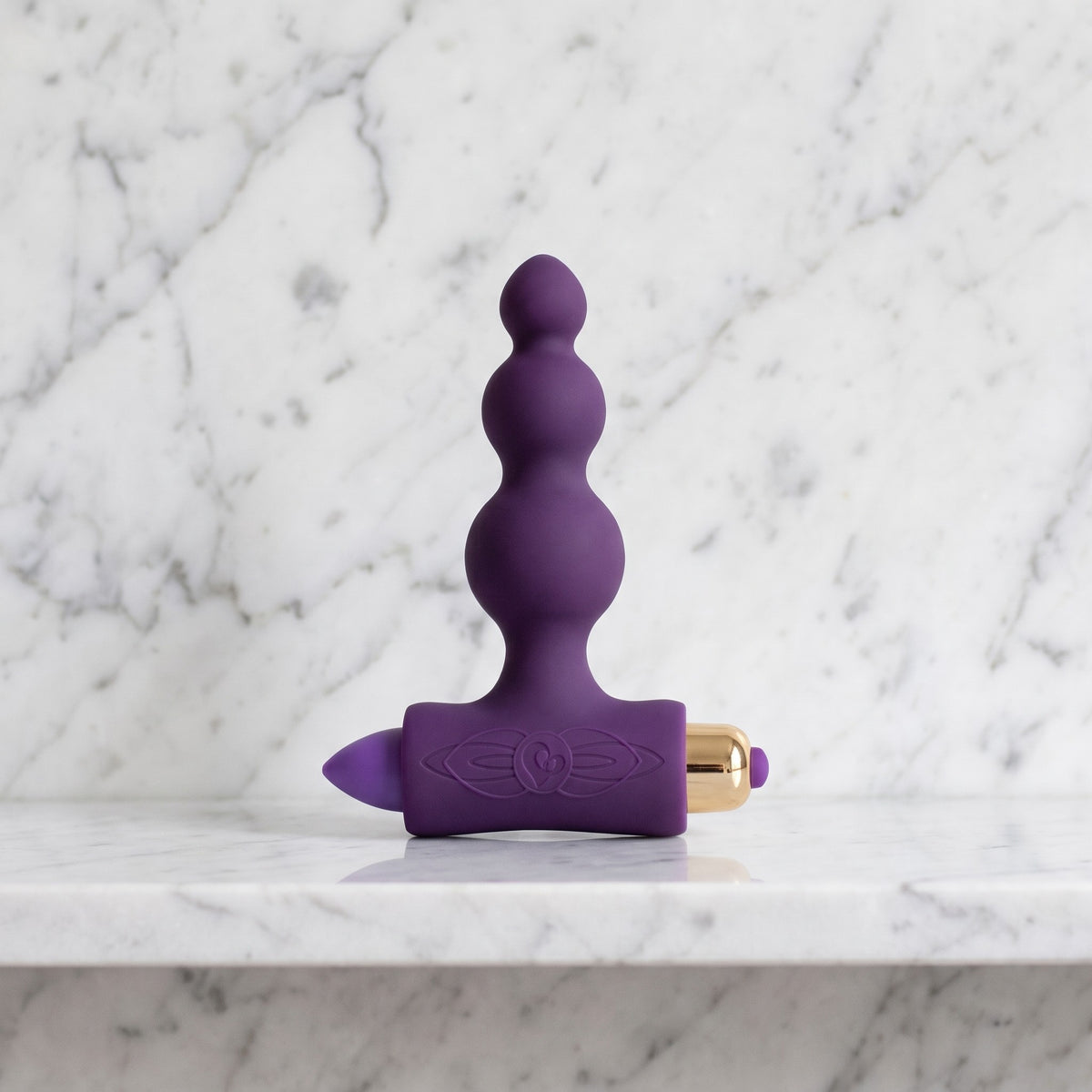 Paarse Petite Sensations Bubble buttplug met drie bolletjes en gouden bullet op een marmeren plank