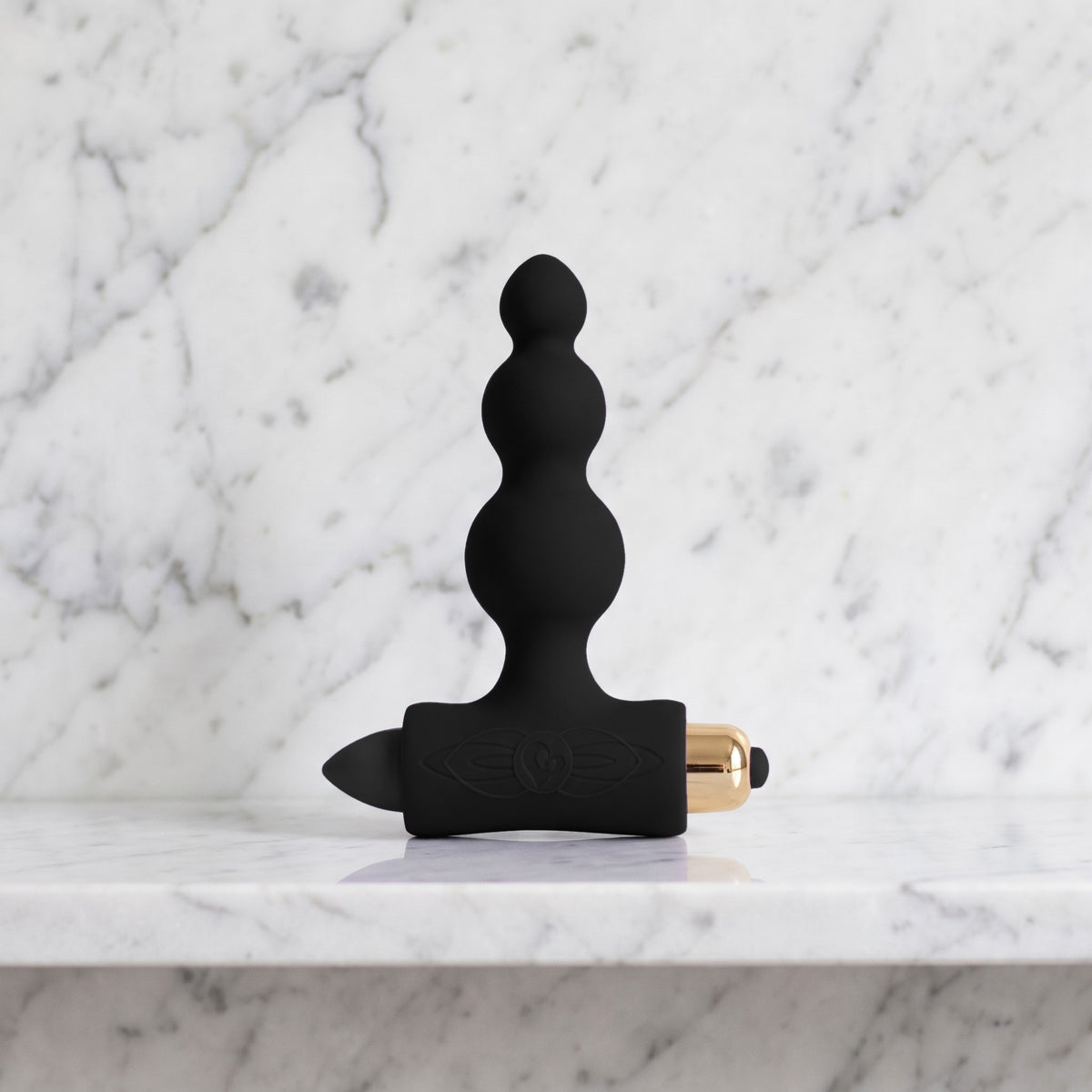 Zwarte Petite Sensations Bubble buttplug met drie bolletjes en gouden bullet op een marmeren plank