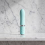 Licht blauwe mini vibrator met ruitjesgreep rechtop op een marmeren plank, Pillow Talk Flirty