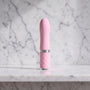 Licht roze mini vibrator met ruitjesgreep rechtop op een marmeren plank, Pillow Talk Flirty