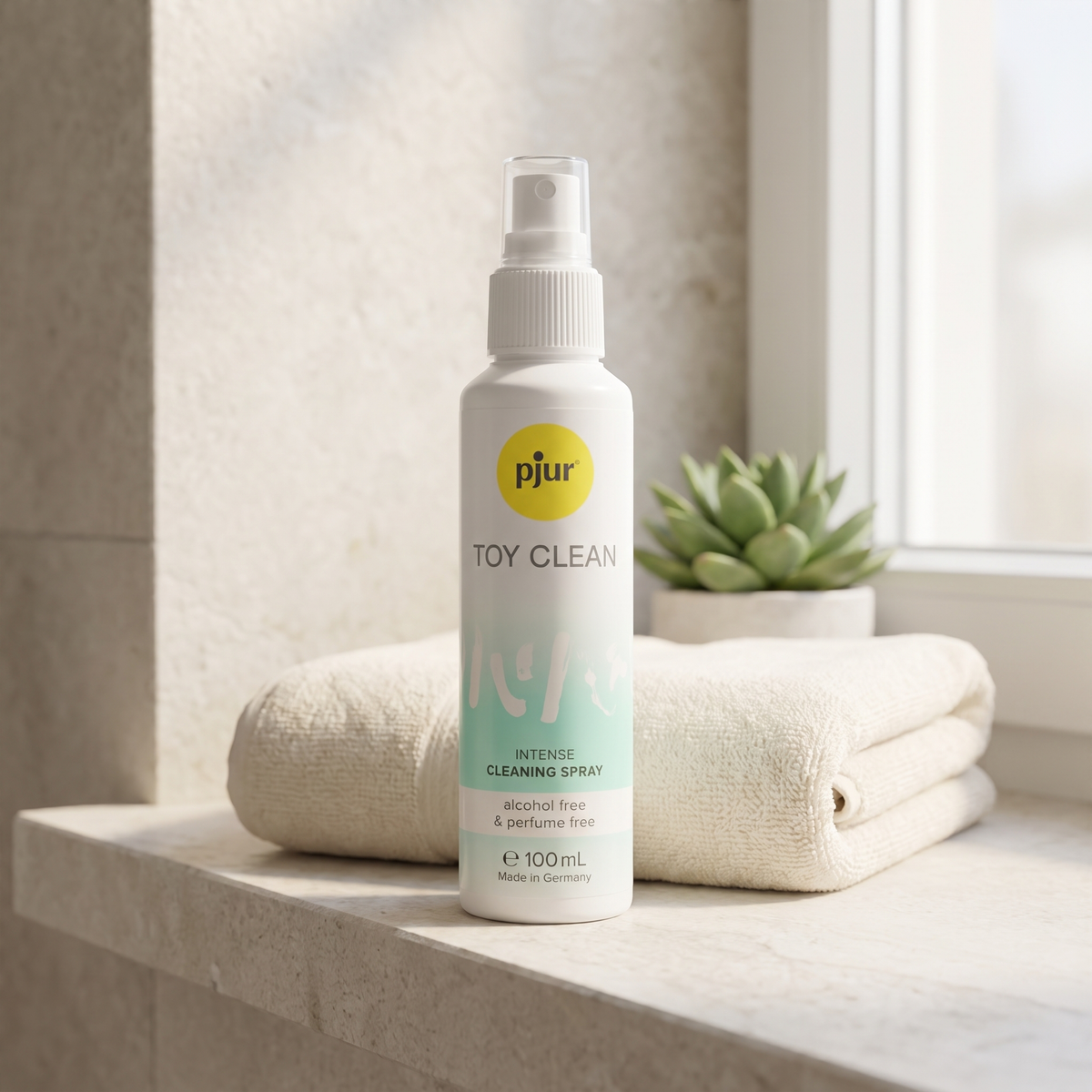 Sfeerbeeld: Pjur Toy Clean rechtop op een badkamerplank naast een opgevouwen handdoek en een vetplant