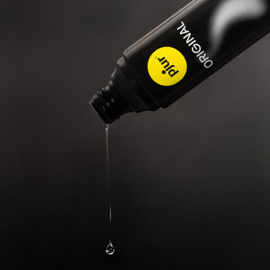 Pjur Original glijmiddel close-up, heldere gel druppelt uit zwarte fles, siliconenbasis textuur