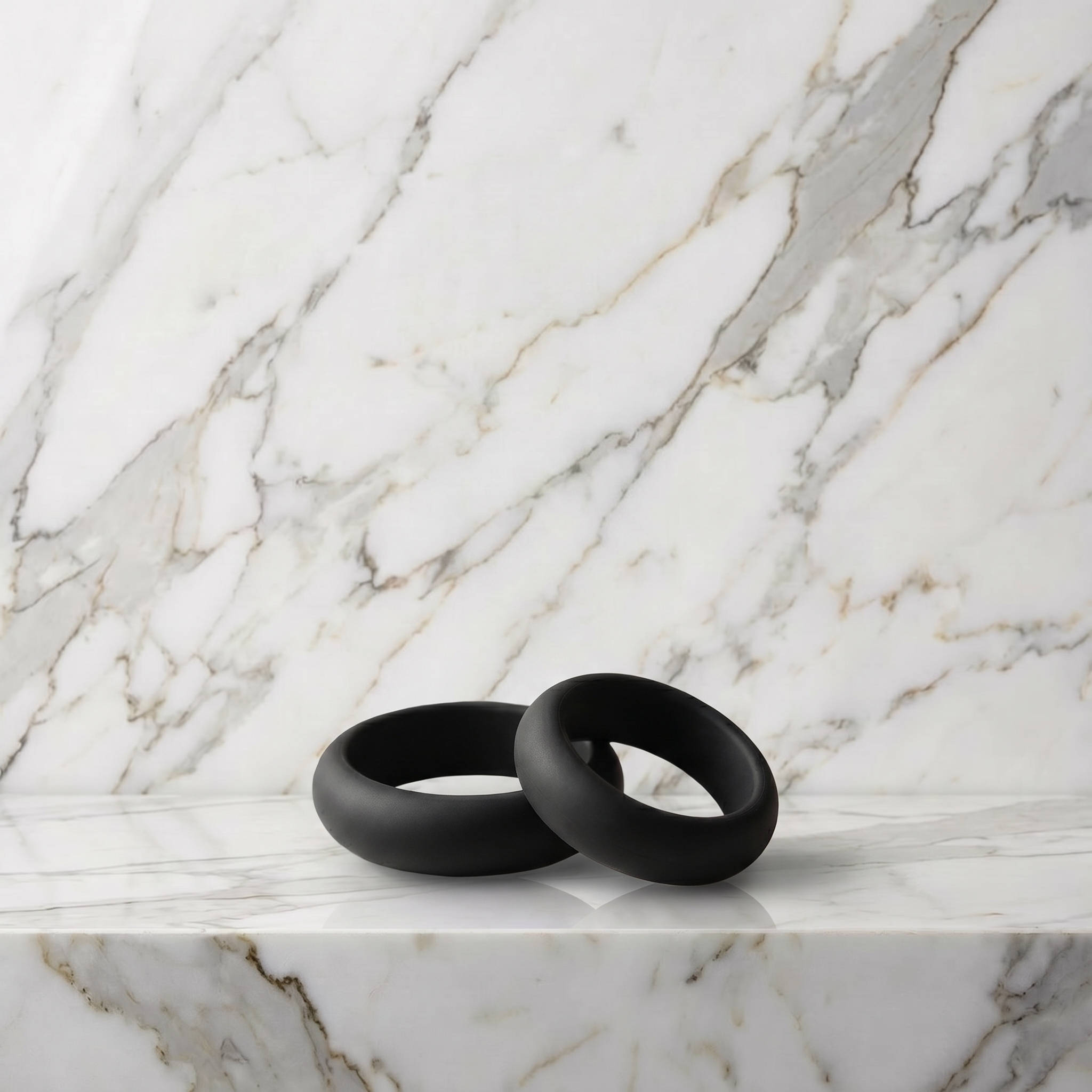 Twee zwarte siliconen cockringen op een marmeren plank, Pleasure Cool Cockringen