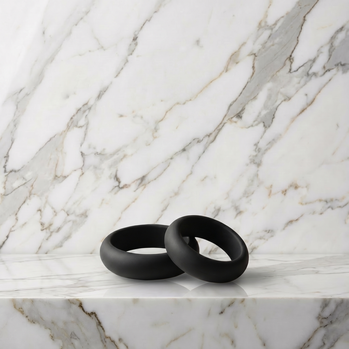 Twee zwarte siliconen cockringen op een marmeren plank, Pleasure Cool Cockringen