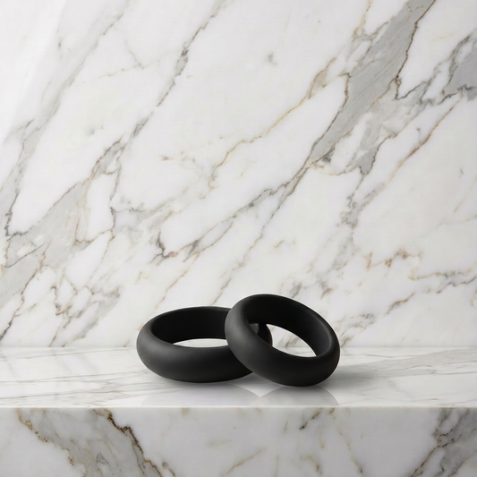 Twee zwarte siliconen cockringen op een marmeren plank, Pleasure Cool Cockringen