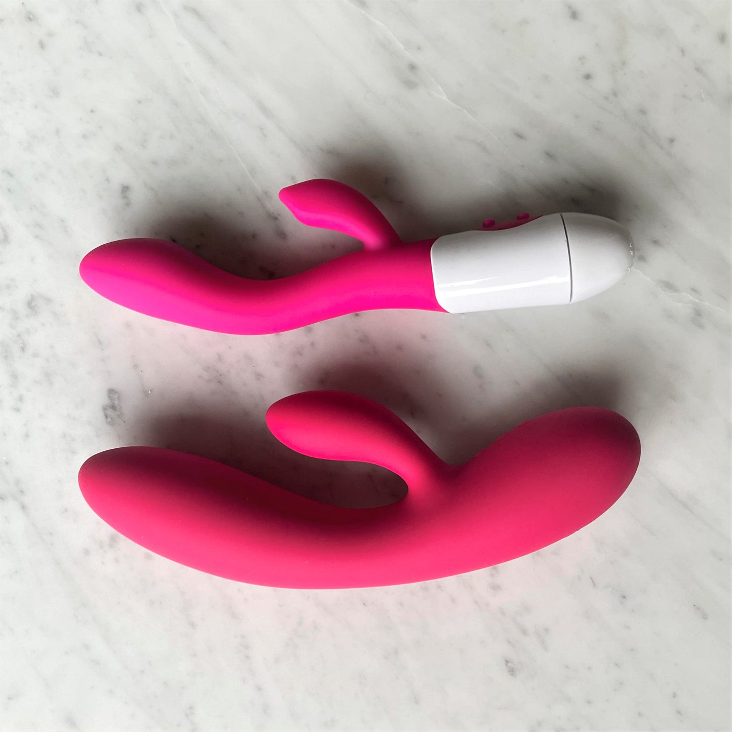 Lily Vibe Easy Toys rabbit vibrator naast gebogen vibrator, beide in roze siliconen op marmer