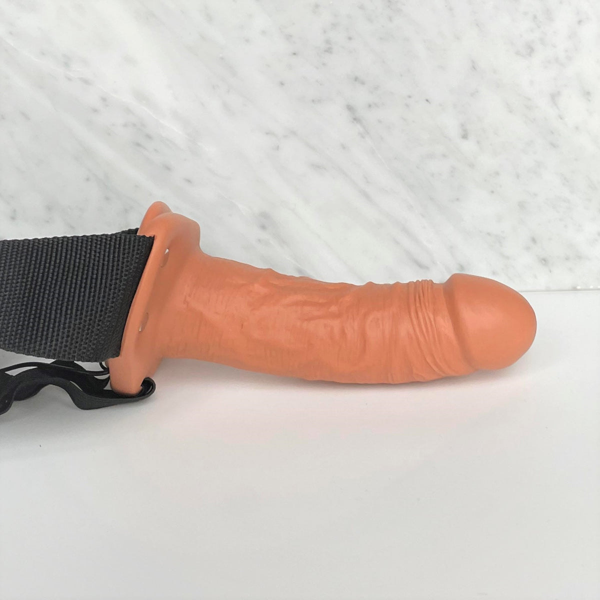 Holle strap-on met zachte tan dildo van 15,5 cm liggend op een marmeren plank