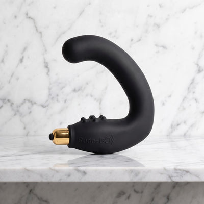 Zwarte Rocks-Off Rude Boy in C-vorm met gouden bullet, prostaatmassager op een marmeren plank