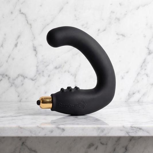 Zwarte Rocks-Off Rude Boy in C-vorm met gouden bullet, prostaatmassager op een marmeren plank
