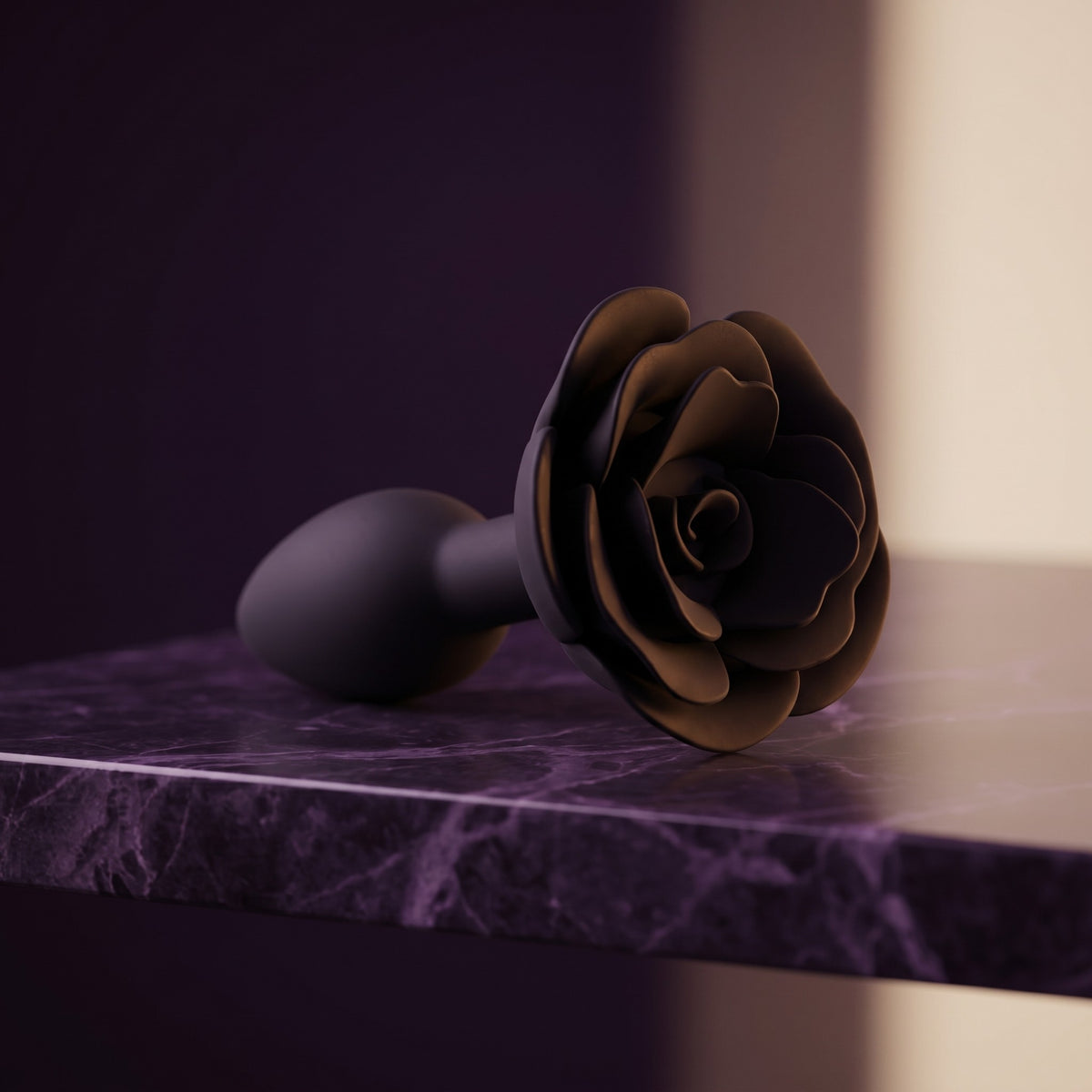 Sfeerbeeld: zwarte Rose buttplug liggend op een donkerpaarse marmeren plank in gedempt licht