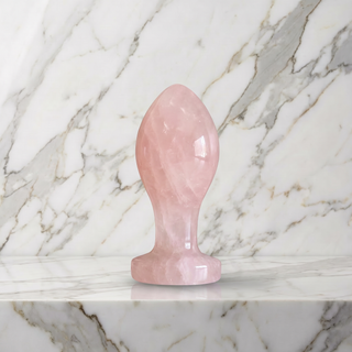 Rozenkwarts Buttplug rechtop op een marmeren plank, lichtroze steen met melkachtige tekening en brede voet