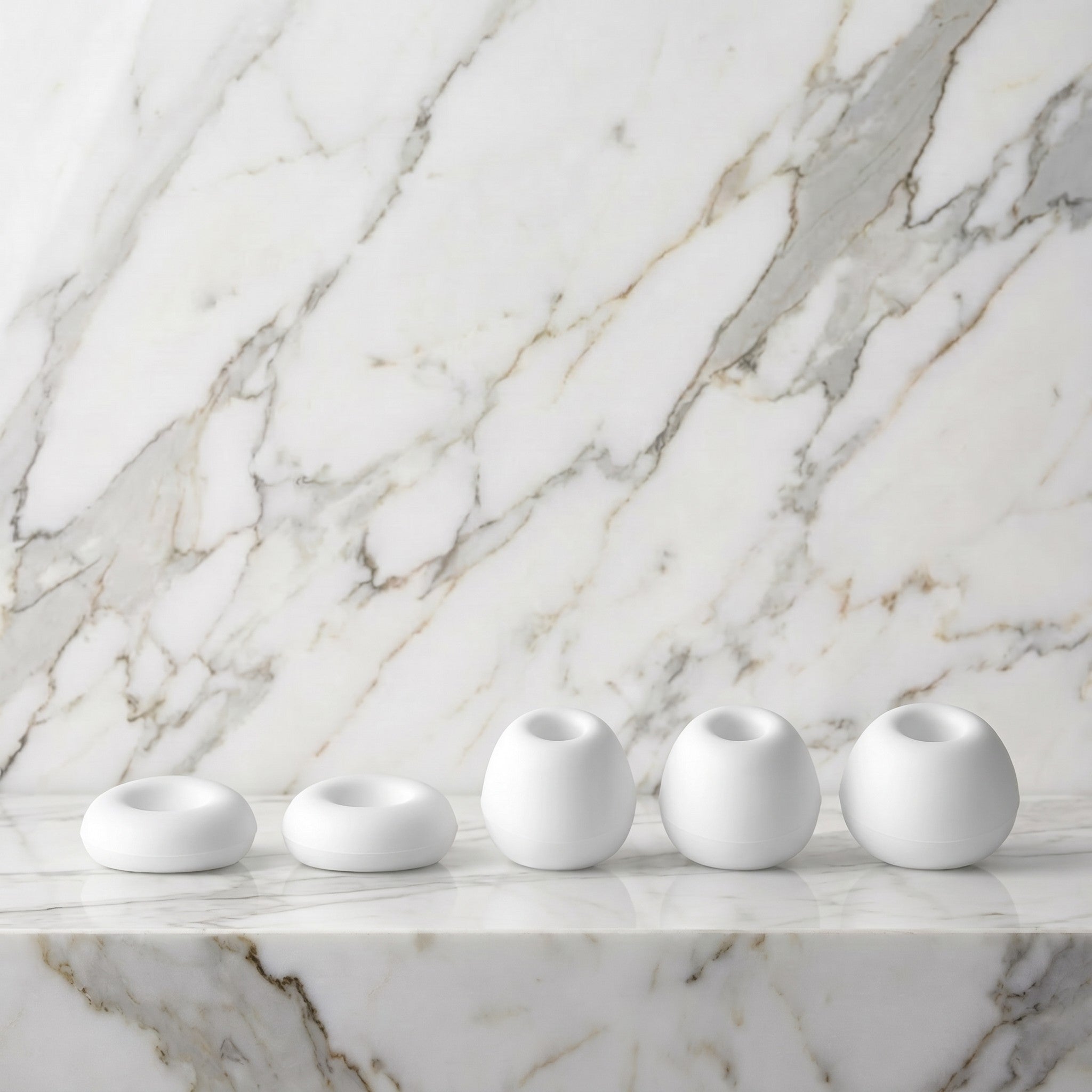 Vijf witte siliconen opzetstukken van de Satisfyer Caps Pro 2 op een marmeren plank
