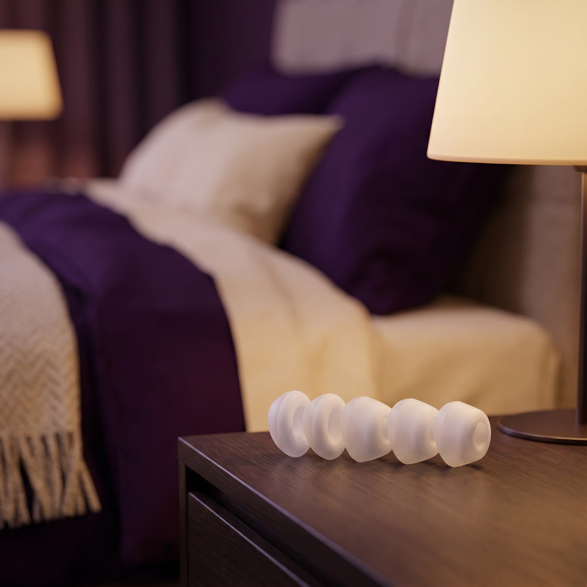 Sfeerbeeld: de vijf opzetstukken van de Satisfyer Caps Pro 2 op een nachtkastje bij lamplicht