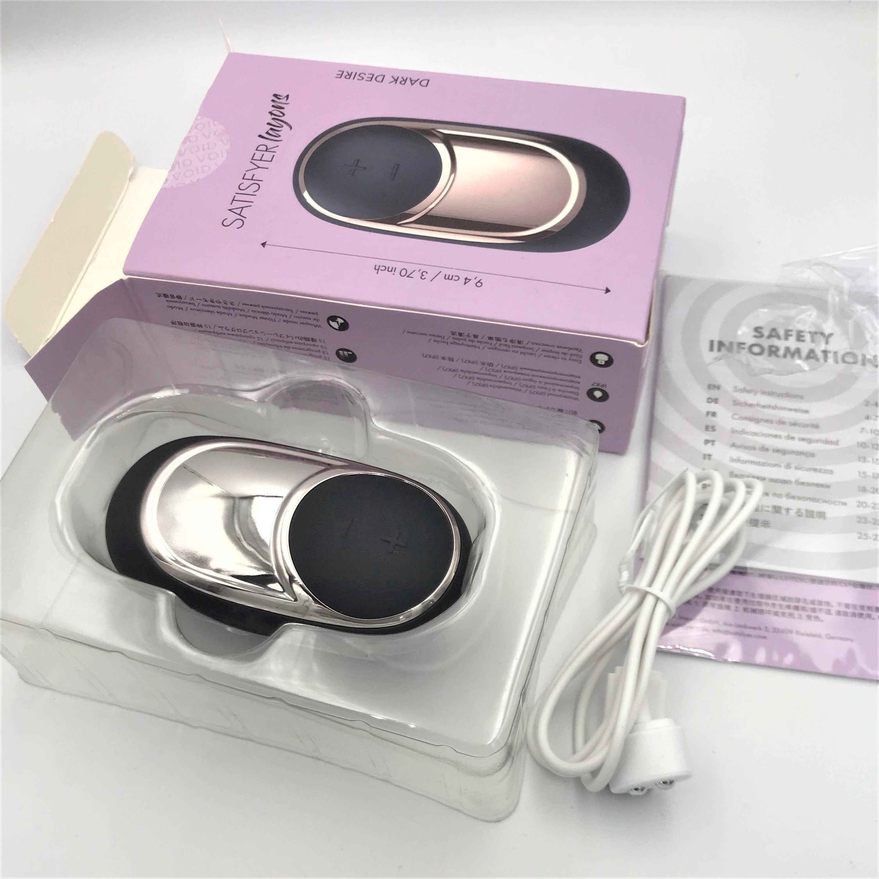 Uitgepakte Satisfyer Dark Desire Layons met doos, oplaadkabel en veiligheidsinformatie