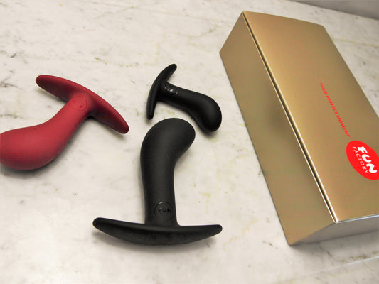 Drie Fun Factory Bootie buttplugs naast gouden geschenkverpakking op marmeren ondergrond