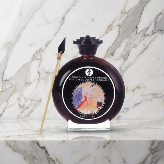 Ronde glazen fles chocolade bodypaint met penseeltje op een marmeren plank, Shunga